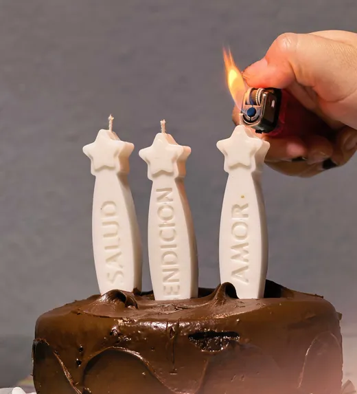 Velas de deseos con forma de estrella y las palabras salud, bendición y amor, encendiéndose sobre un pastel